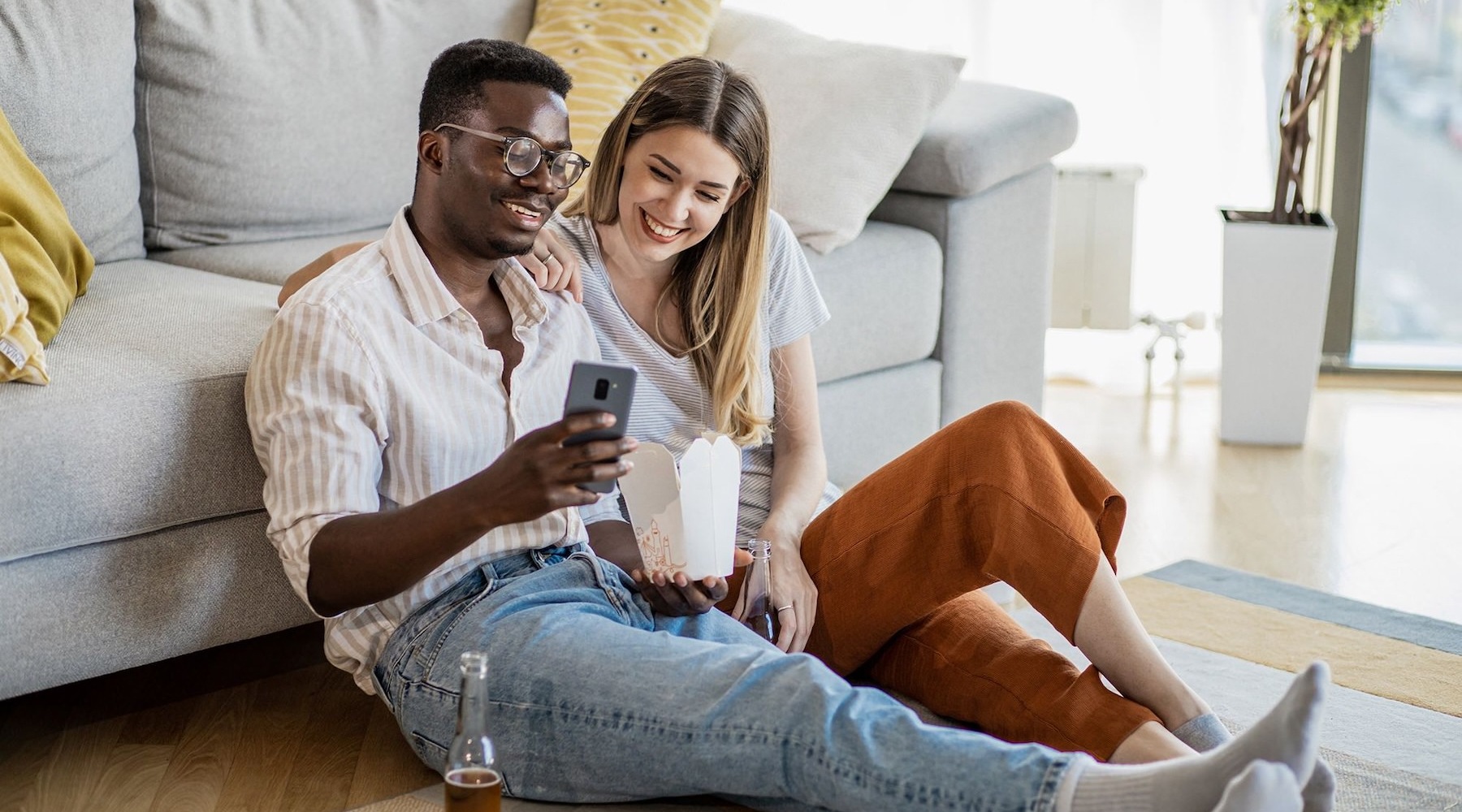 A couple sitting in front of a couch two people sitting down in front of a couch in a living room